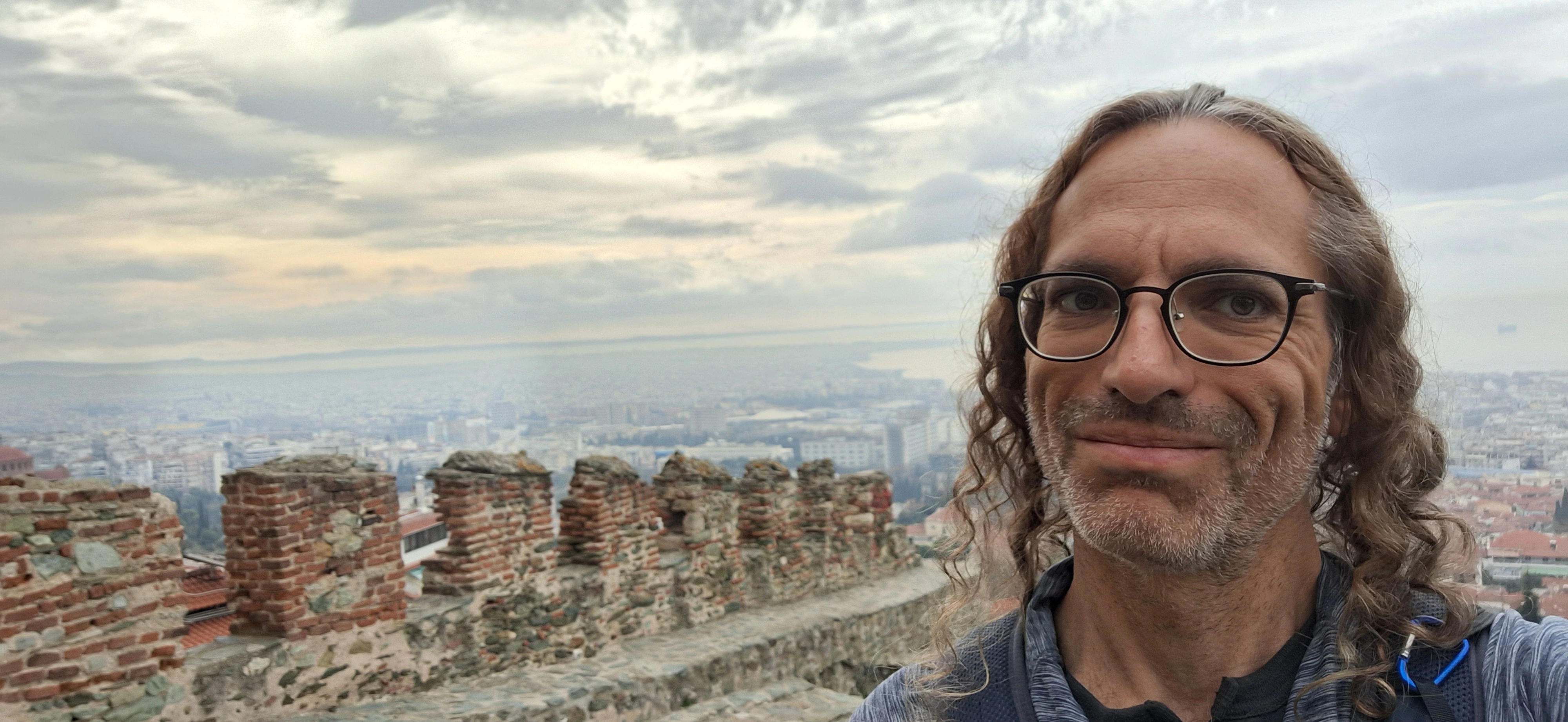 Richard Massel walking along historic stone fortress walls overlooking a city in Greece.