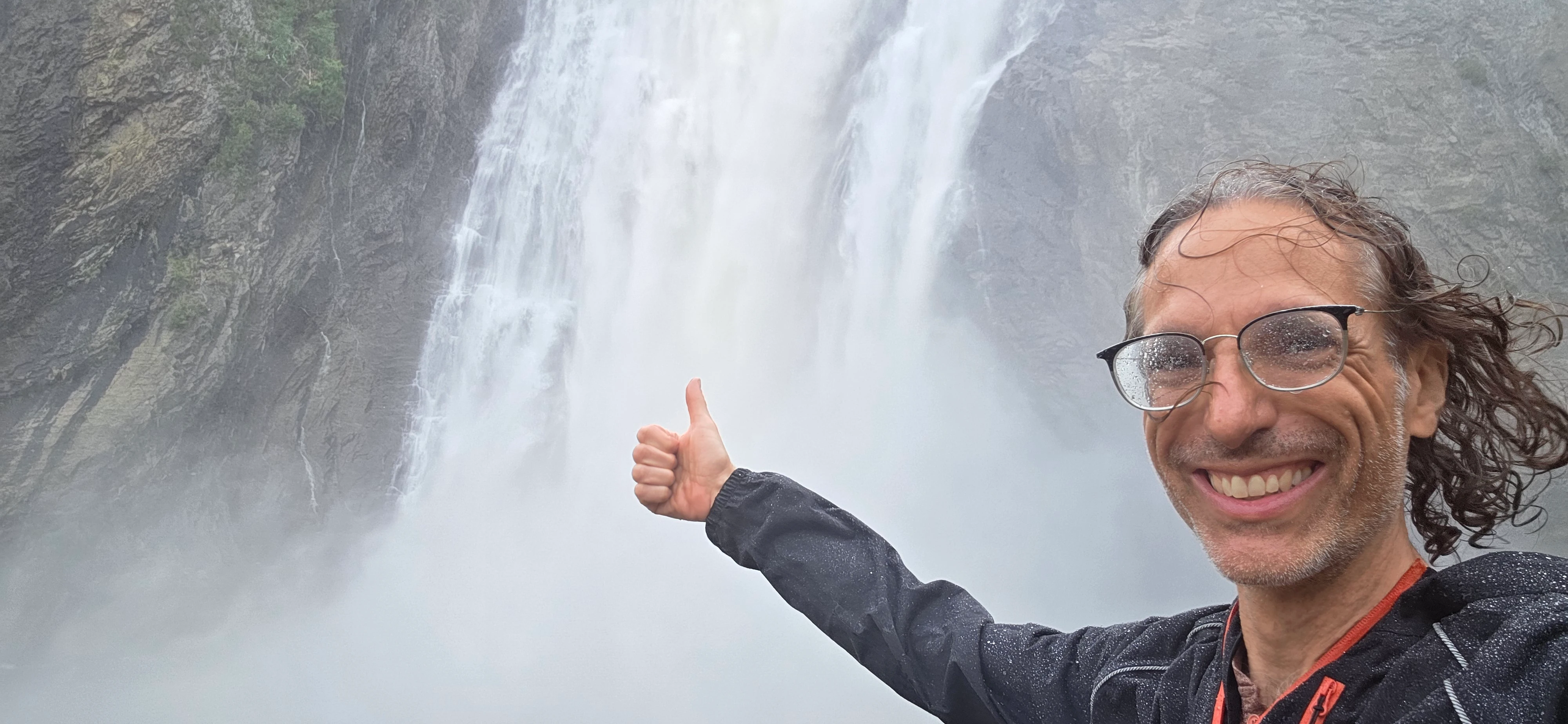 Richard Massel giving a thumbs up in front of a large waterfall.